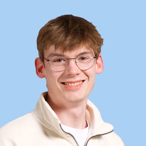 Tommy, the designer behind Paper Plane, smiling in a cream jacket and round glasses.