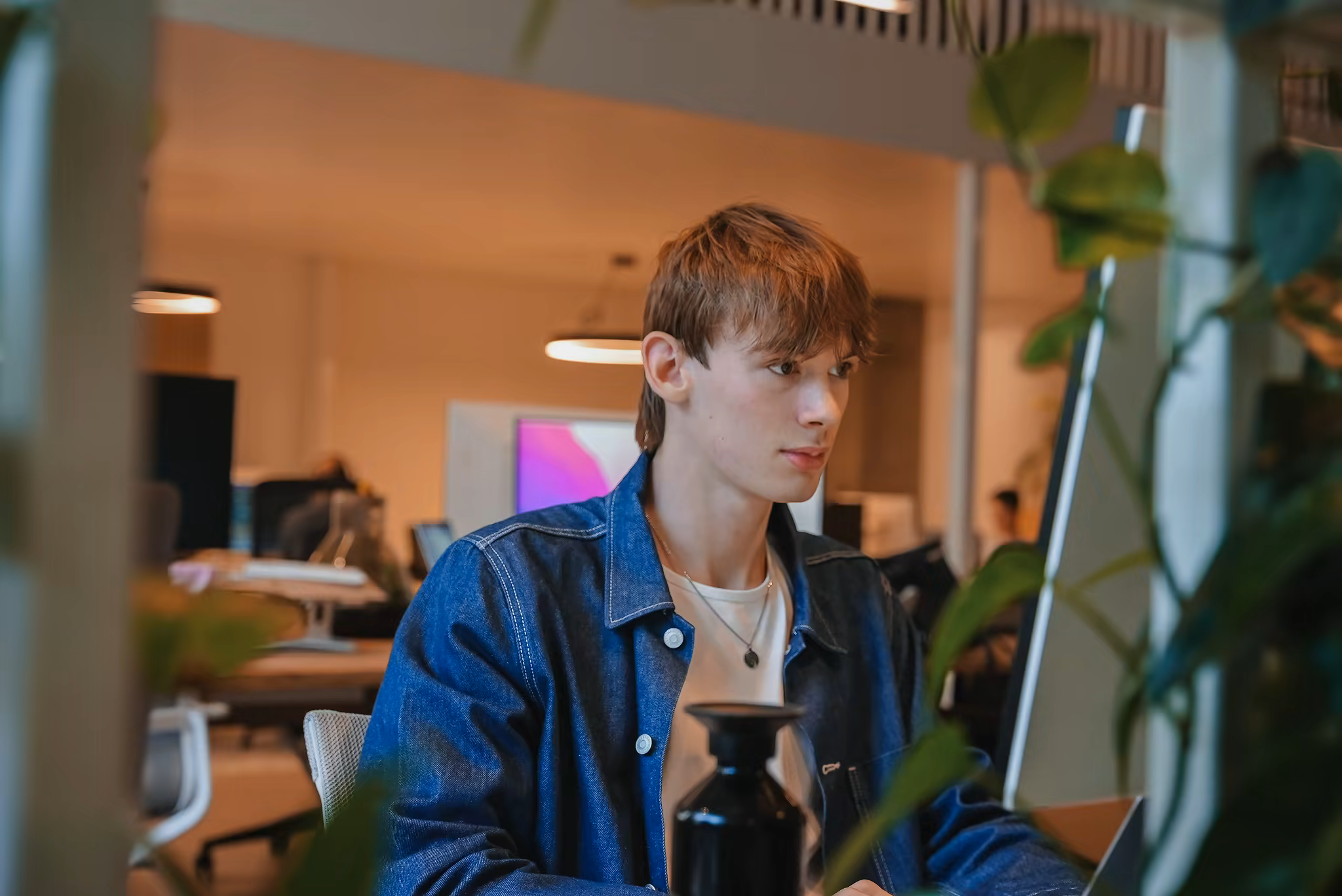 Tommy working at a desk in a bright office, focused on a large screen.